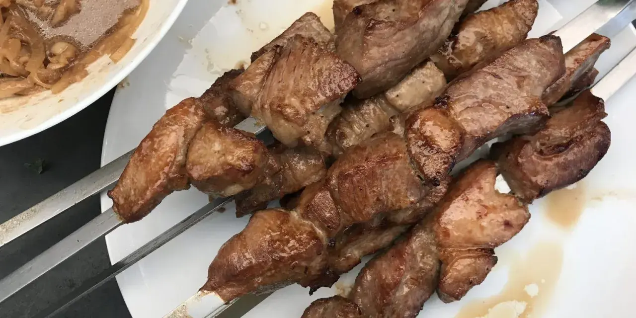Saftige Fleischspieße, perfekt gegrillt, wie beim besten russischen Schaschlik Rezept. Dazu eine Schüssel mit marinierten Zwiebeln.