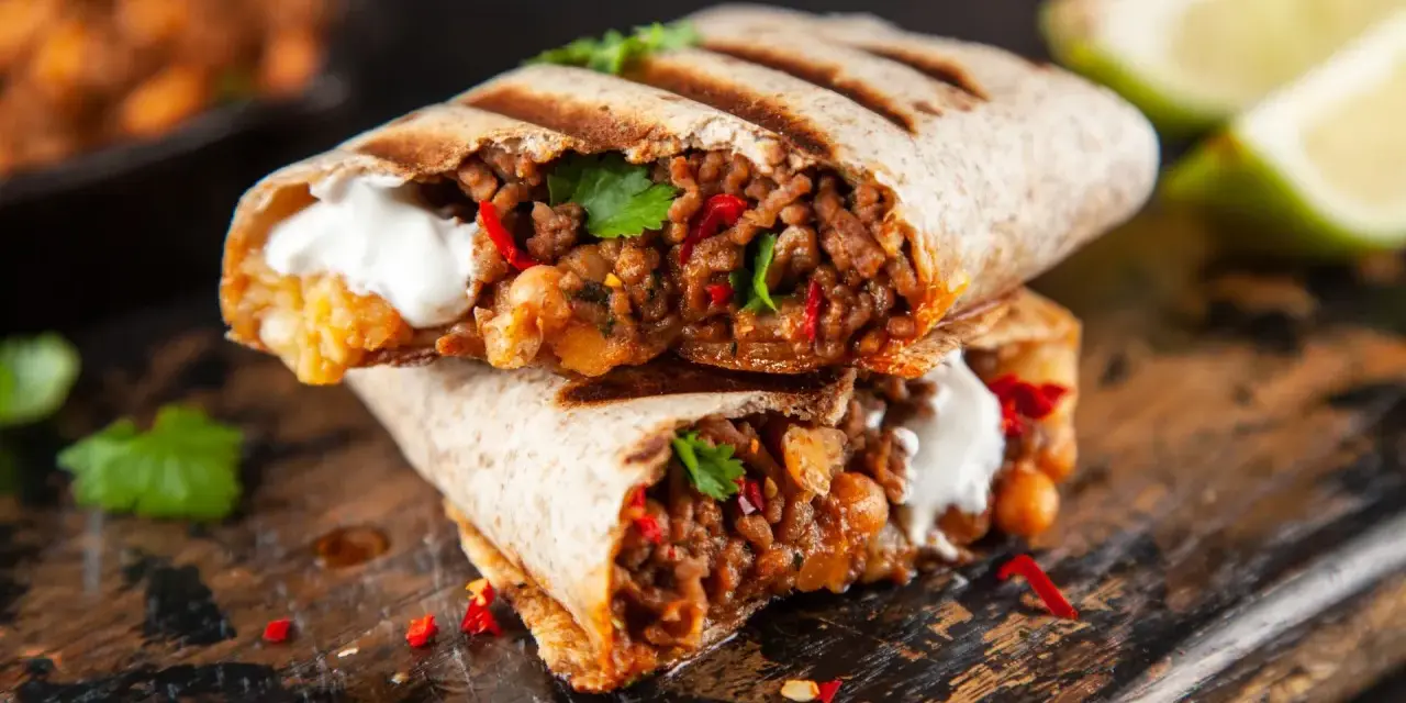 Zwei saftige Burritos, gefüllt mit Hackfleisch, Bohnen und einem Klecks Sauerrahm, sind ein köstliches burrito rezept. Garniert mit Koriander und Chili.