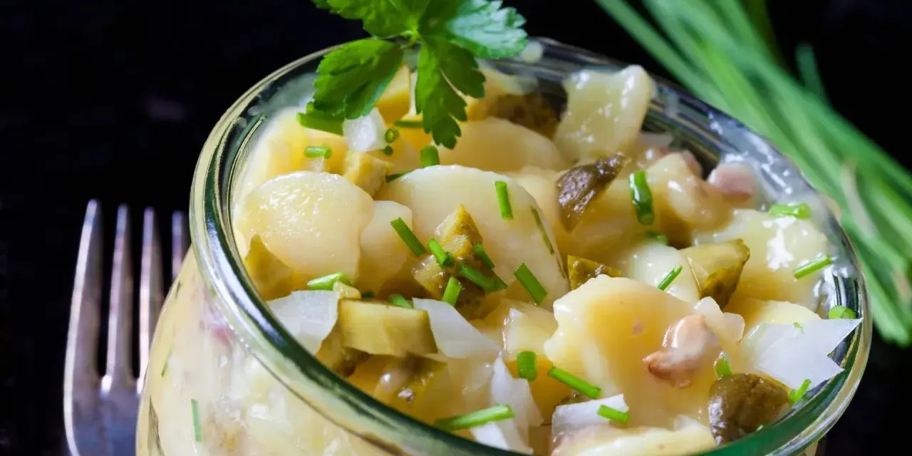 Ein köstlicher Kartoffelsalat ohne Mayo, mit Gurken, Zwiebeln und frischen Kräutern, serviert in einem Glas.