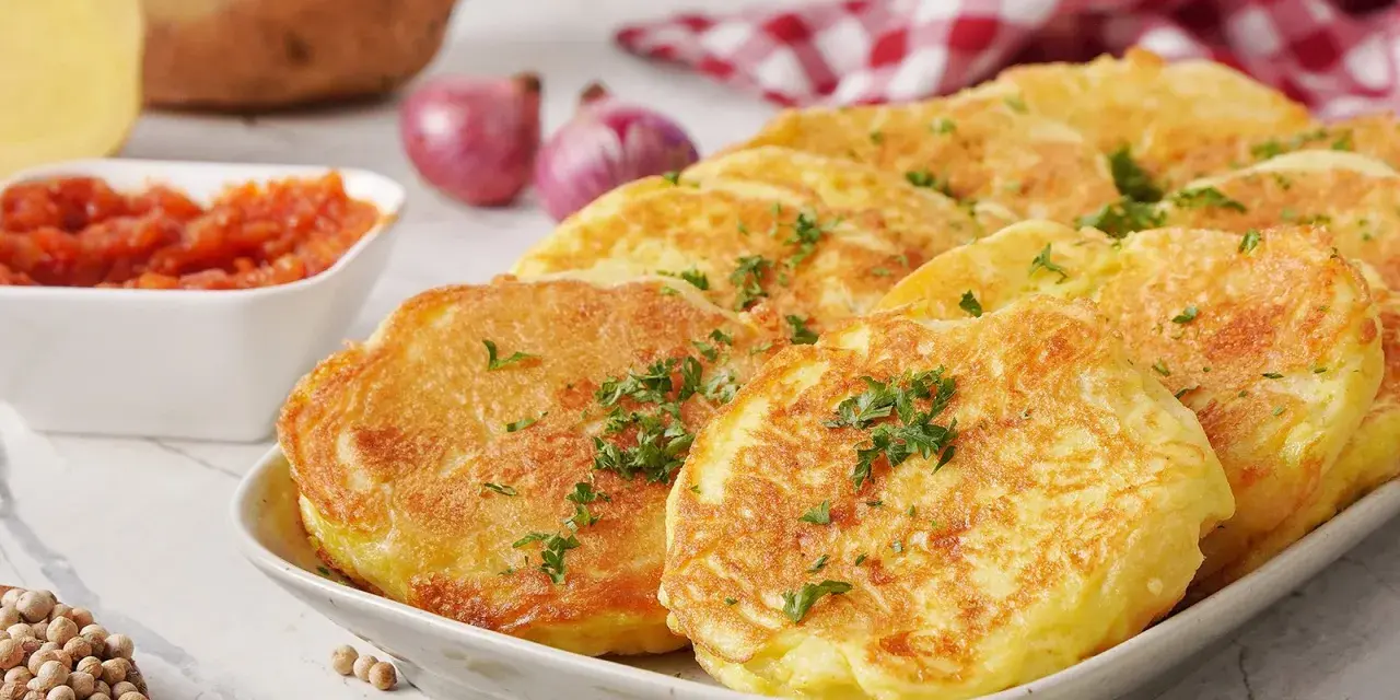 Goldbraune Kartoffelpuffer, garniert mit Petersilie, sind ein köstliches Beispiel für Rezepte mit Kartoffeln als Hauptspeise. Dazu passen Tomatensoße und Zwiebeln.