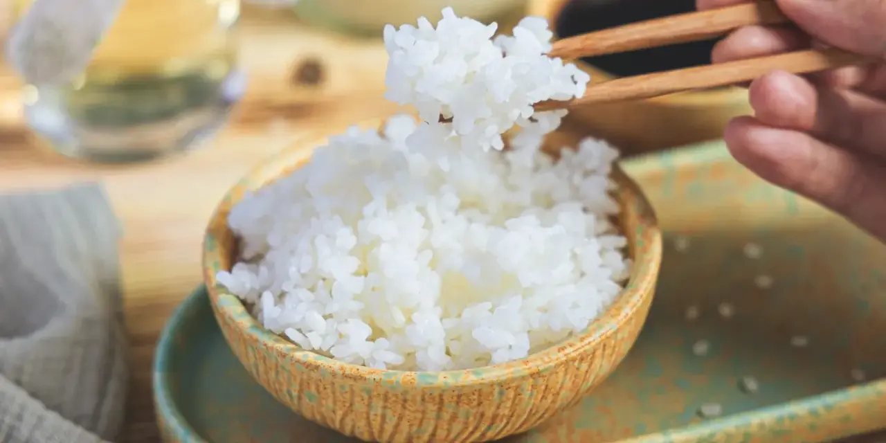 Perfekter sushi reis im reiskocher, dampfend und bereit, mit Stäbchen gegriffen zu werden. Ein Hauch von Asien auf dem Tisch.