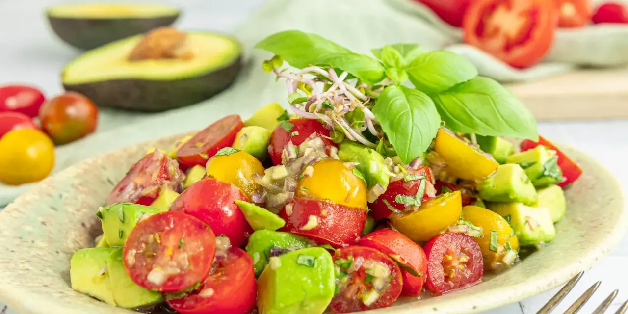 Frischer Avocado Tomaten Salat mit Basilikum und Sprossen, garniert mit roten und gelben Kirschtomaten.
