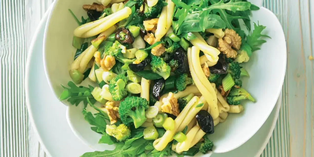 Frischer nudelsalat mit brokkoli, Walnüssen, Oliven und Rucola in einer weißen Schüssel.