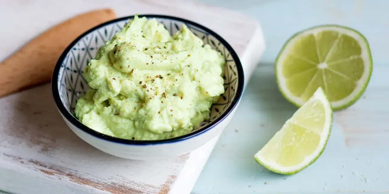 Cremiger Avocado Feta Dip, gewürzt mit Pfeffer, daneben frische Limettenspalten. Perfekt zum Dippen!