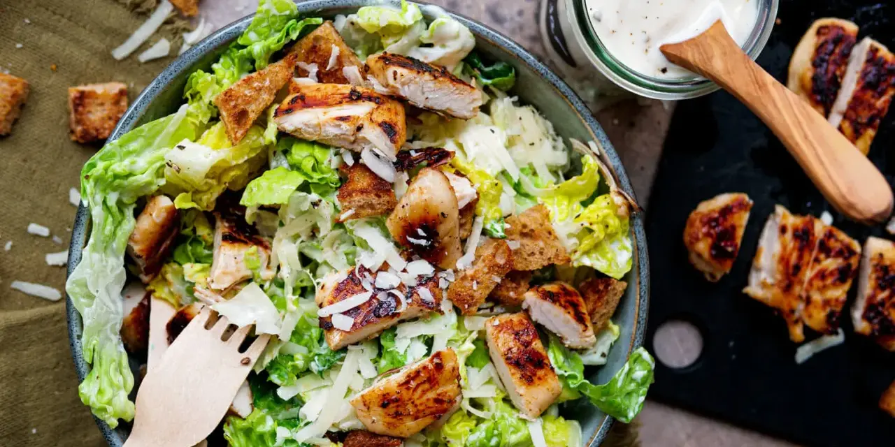 Frischer Caesar Salat mit gegrilltem Hähnchen, Croutons und Parmesan. Dazu ein Glas mit cremigem Caesar Salat Dressing.