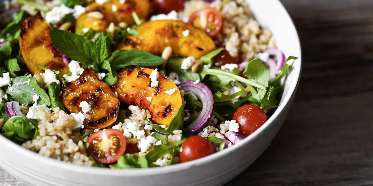 Ein bunter Pfirsich Feta Salat mit gegrillten Pfirsichspalten, Kirschtomaten, Rucola und Getreide.
