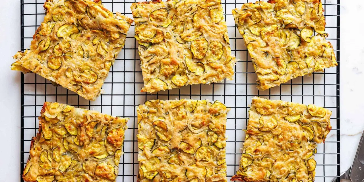 Sechs rechteckige Stücke Zucchini Scarpaccia liegen auf einem schwarzen Gitterrost.