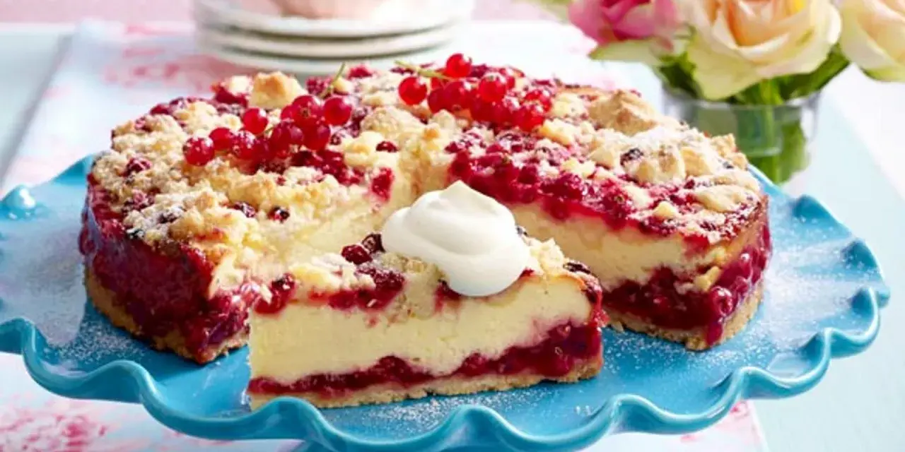 Saftiger Johannisbeerkuchen mit Quark und Streuseln, garniert mit frischen roten Johannisbeeren und einem Klecks Sahne.