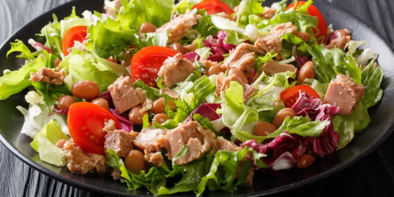 Frischer Thunfischsalat mit knackigem Salat, Tomaten und Bohnen auf schwarzem Teller.