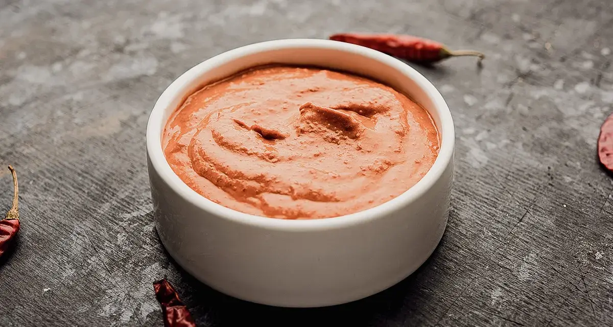 Eine Schale mit cremiger Piri Piri Sauce, umgeben von getrockneten Chilis auf dunklem Untergrund.