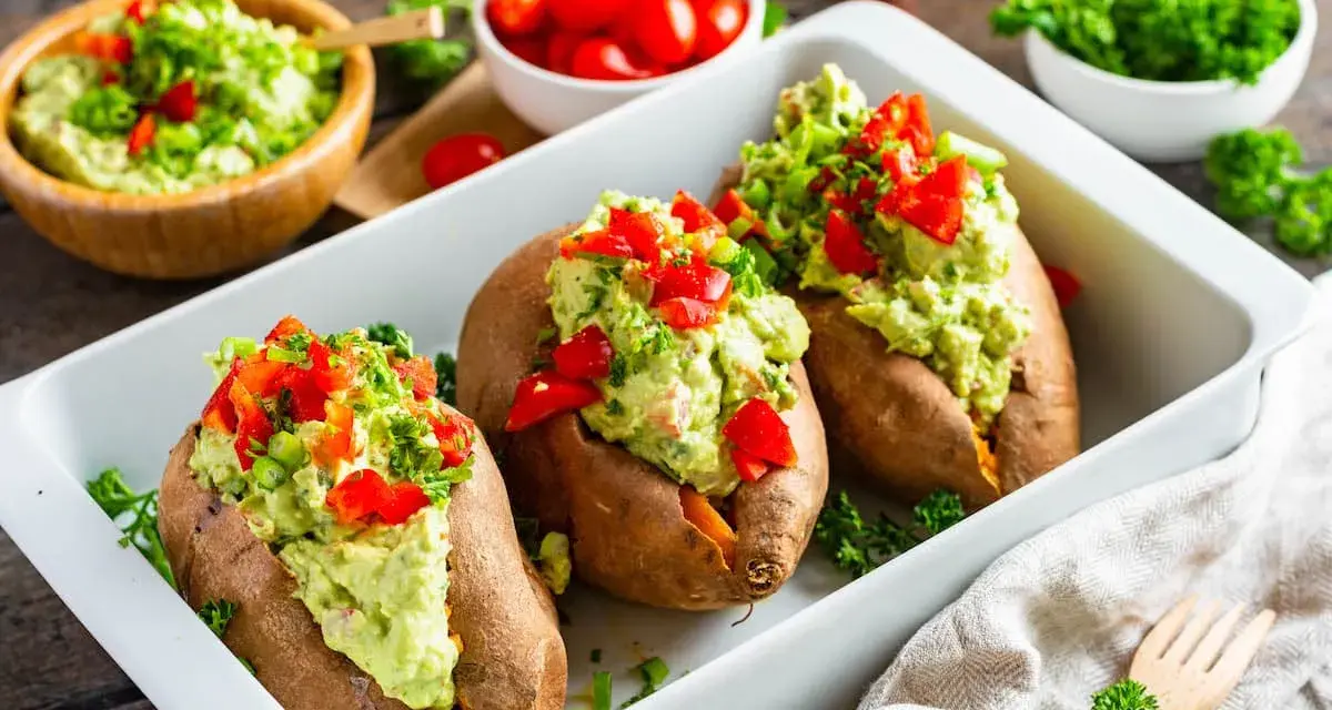 Gefüllte Süßkartoffeln mit Avocado-Topping. Leckere, kalte Rezepte mit Avocado, garniert mit Paprika und Kräutern.