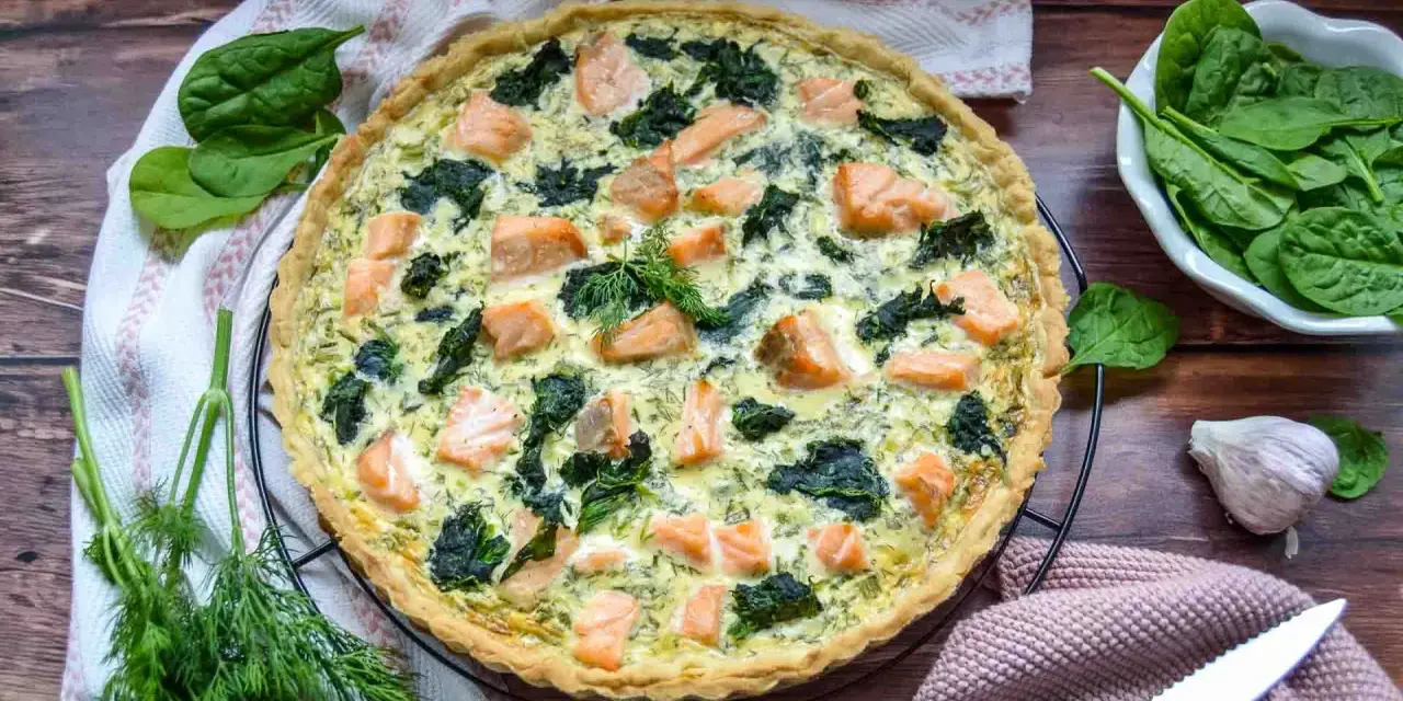 Herzhafte Spinat Lachs Quiche mit frischem Dill garniert, bereit zum Servieren.