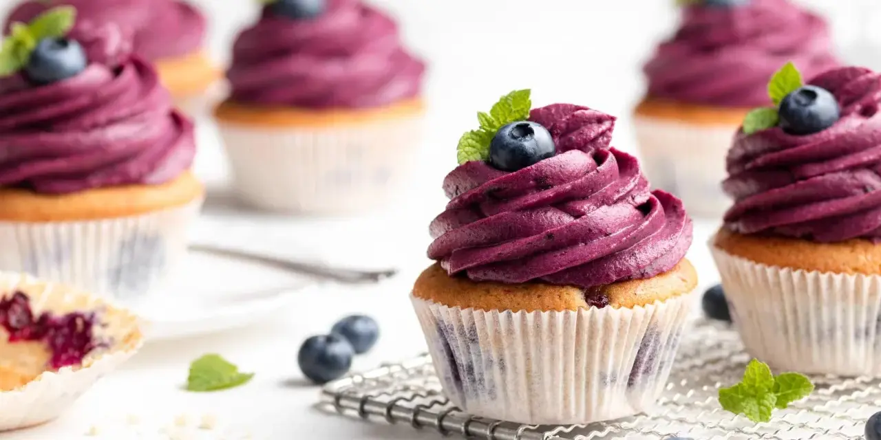 Mehrere Muffins mit lila Beeren-Topping, garniert mit frischen Blaubeeren und Minze. Ein einfacher, köstlicher Genuss.