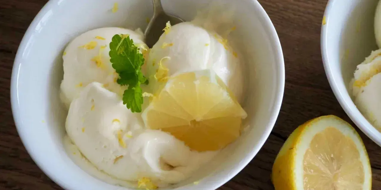 Erfrischendes zitroneneis selber machen: Cremiges Eis in einer Schüssel, garniert mit Zitronenspalte und Minze.