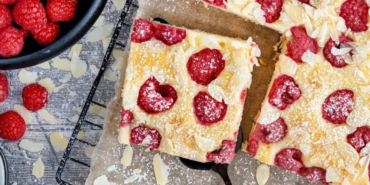 Schneller Kuchen mit gefrorenen Himbeeren, bestreut mit Puderzucker und Mandelblättchen. Ein Genuss für jeden Anlass!