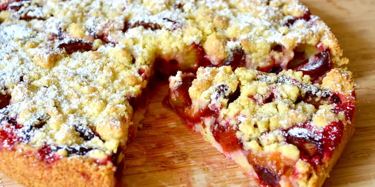 Saftiger pflaumenkuchen ohne hefe springform, mit Streuseln und Puderzucker bestäubt, auf einem Holzbrett.