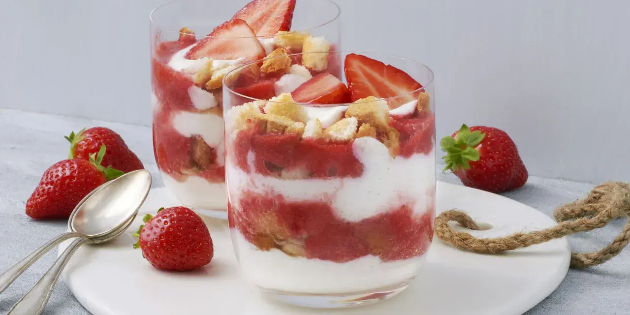 Zwei Gläser mit einem sommerlichen Dessert aus Erdbeeren und Sahne, garniert mit frischen Erdbeeren und Keksen. Ein schnell und einfach zubereitetes Genusserlebnis.