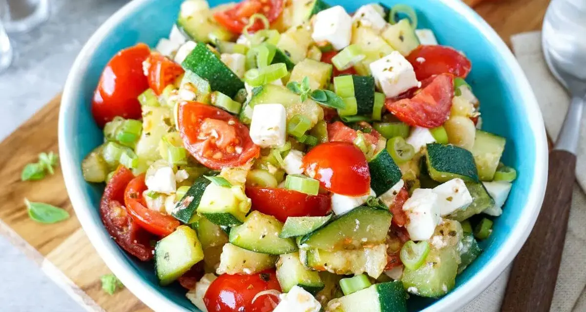 Erfrischender Zucchini Salat mit Tomaten, Feta und Frühlingszwiebeln, garniert mit frischen Kräutern. Ein leichter Genuss.