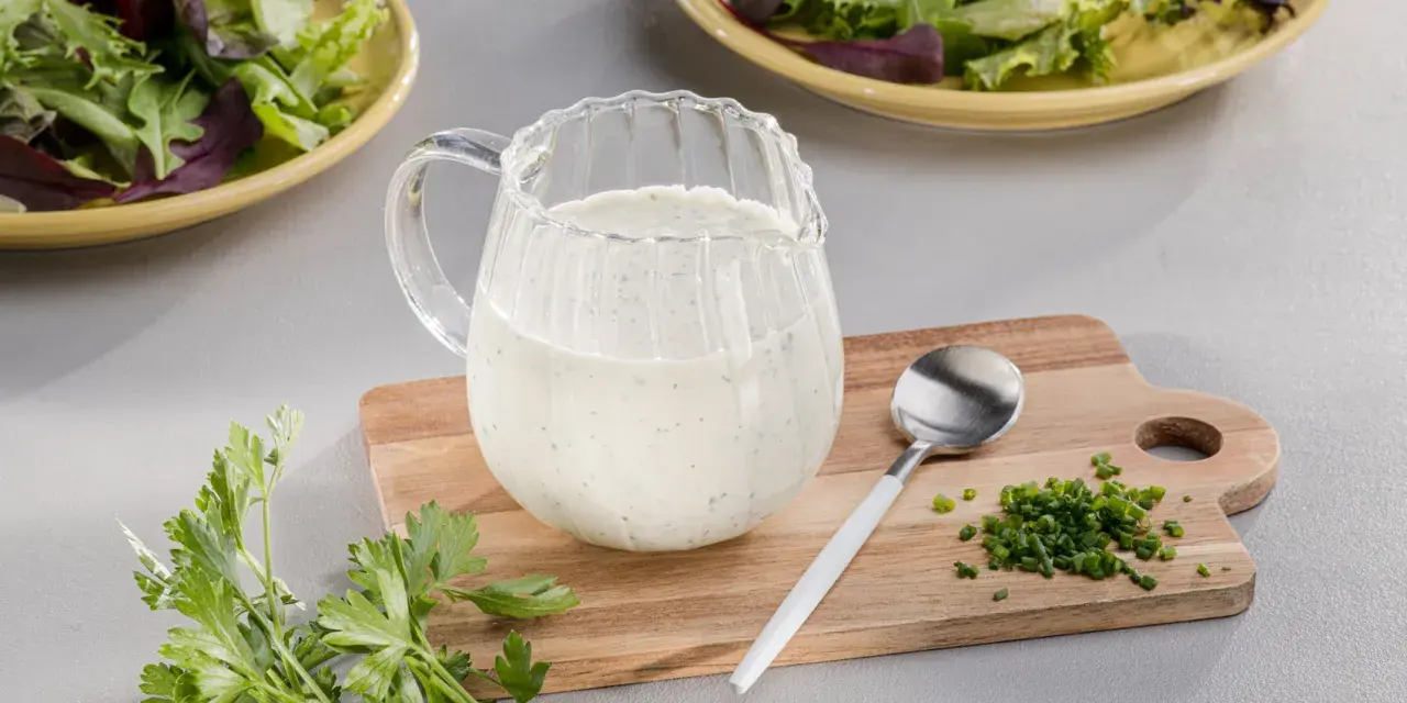 Ein Krug mit cremigem Ranch Dressing, daneben Schnittlauch und Petersilie. Perfekt für einen frischen Salat.