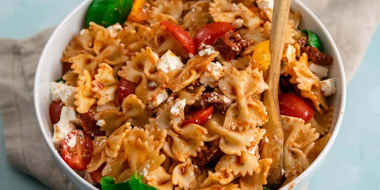 Ein köstlicher Nudelsalat mit Farfalle, frischen Tomaten, Mozzarella und sonnengetrockneten Tomaten, garniert mit Basilikum.