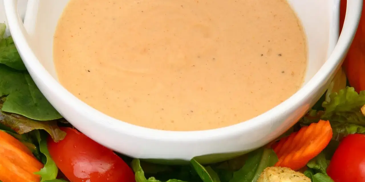 Cremiges French Dressing in einer weißen Schüssel, umgeben von frischem Salat, Tomaten und Karotten.