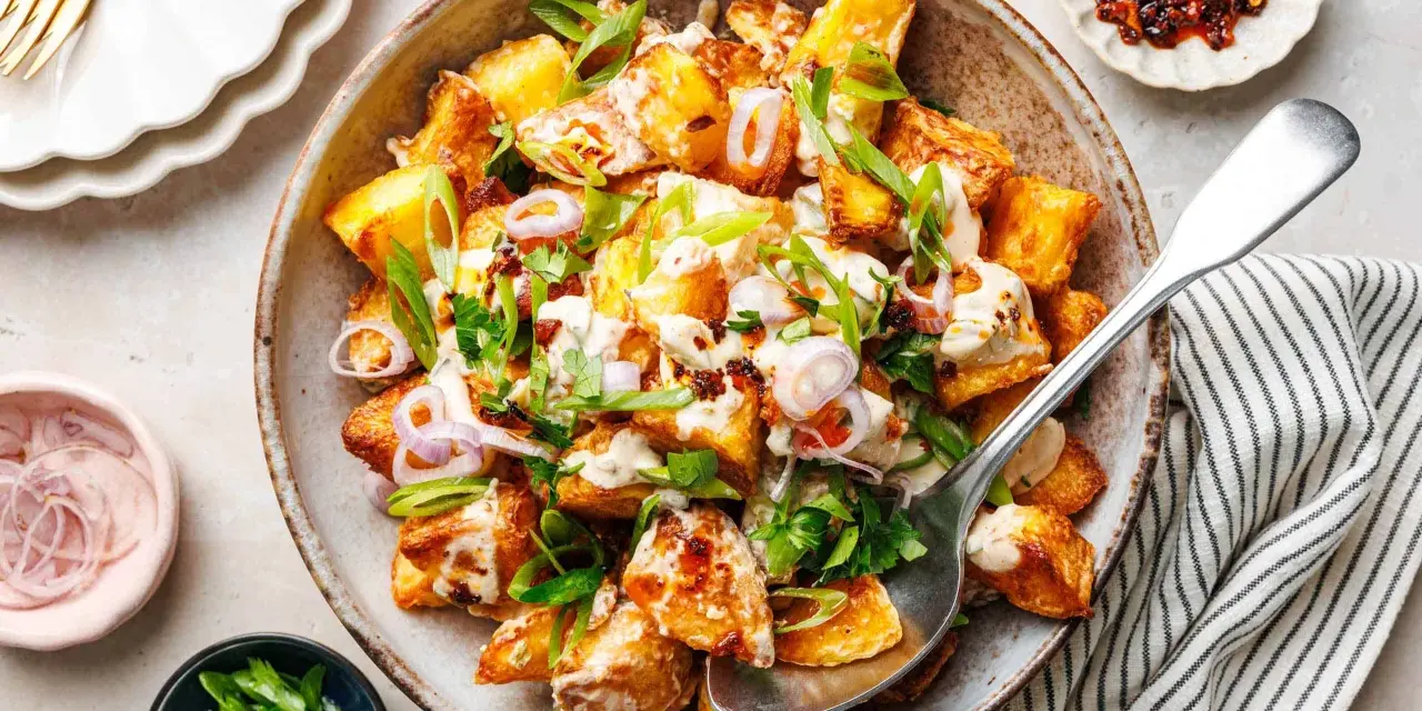 Kartoffelsalat mal anders: knusprige Kartoffelspalten mit cremiger Sauce, Frühlingszwiebeln und roten Zwiebelringen in einer rustikalen Schüssel.