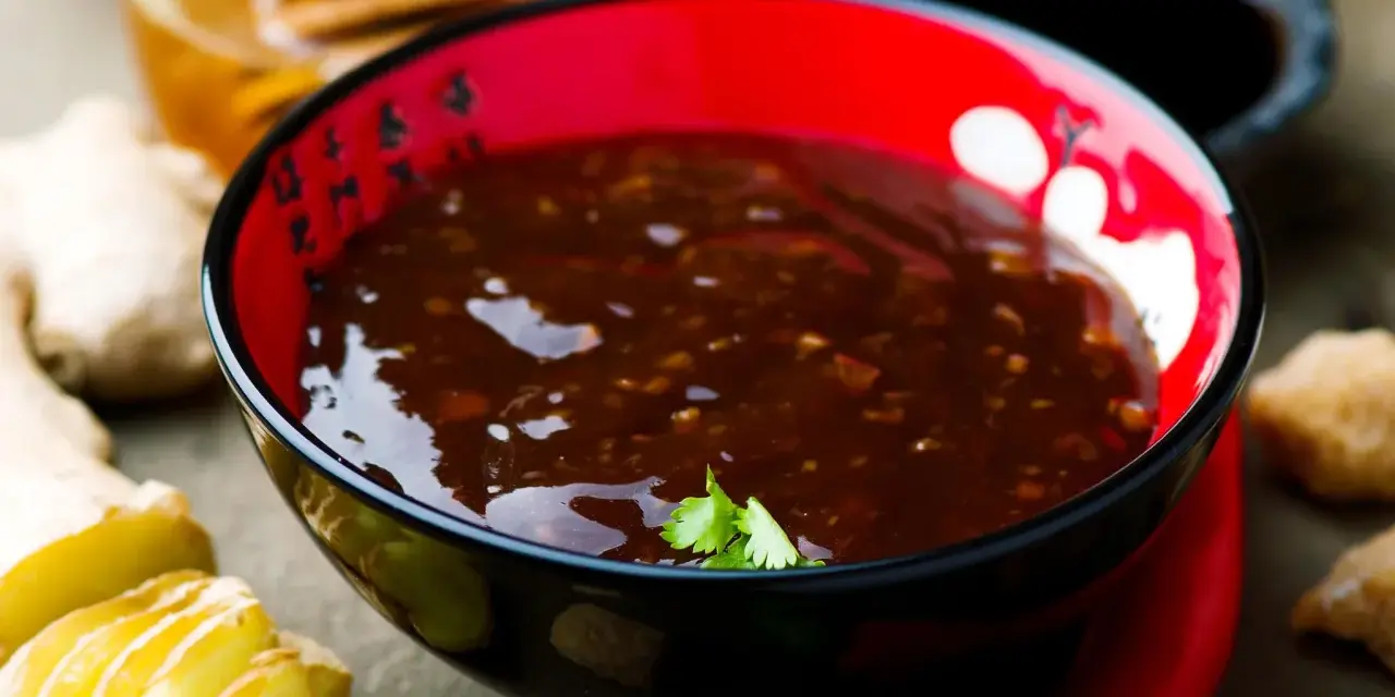 Schwarze Schüssel mit glänzender Teriyaki-Sauce, umgeben von Ingwer, Knoblauch und Chili. Ein köstliches teriyaki sauce rezept zum Nachkochen.