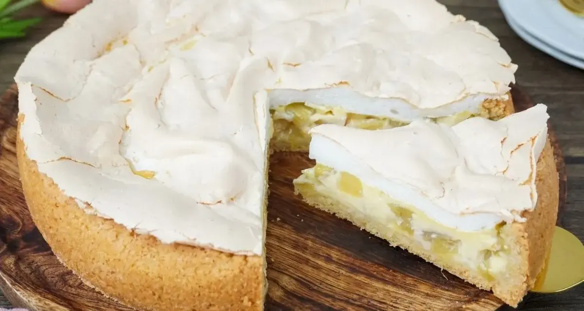 Ein saftiger Rhabarberkuchen mit luftigem Baiser, ein Stück davon ist bereits angeschnitten.