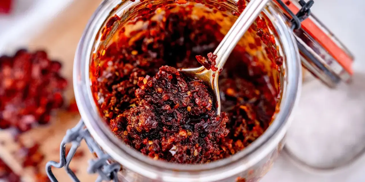 Ein Glas mit würzigem Chili Crunch, perfekt für jedes Chili Crunch Rezept. Eine Löffelspitze voller Geschmack!