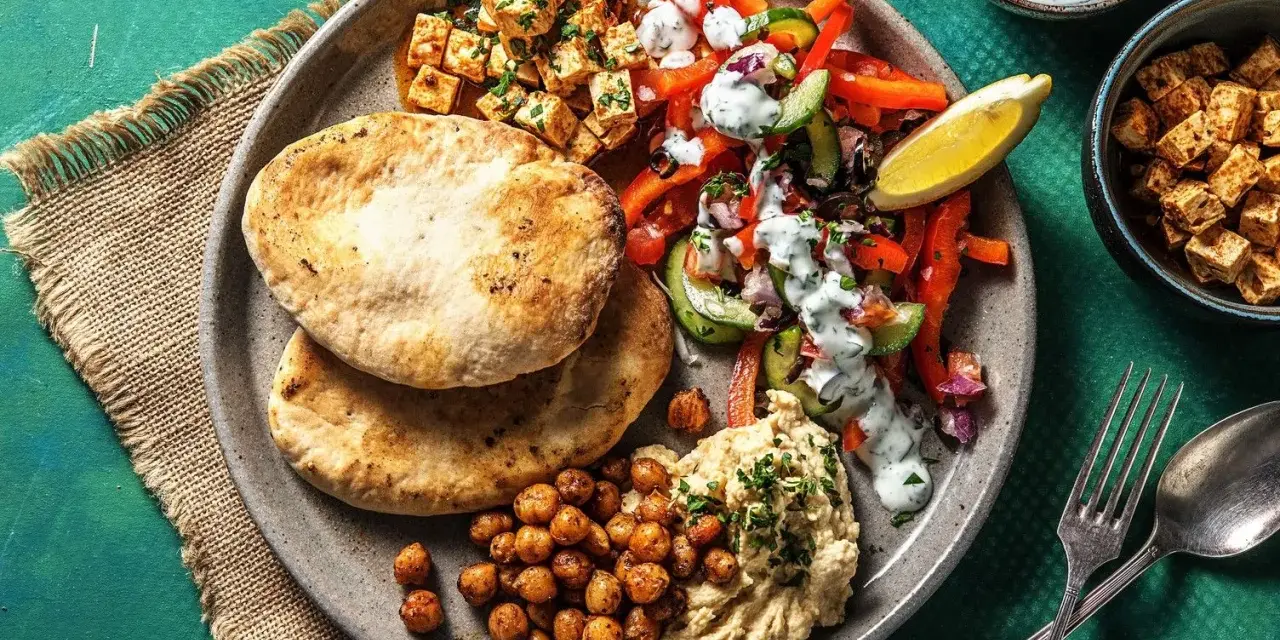 Ein bunter griechischer Salat mit Hummus, gerösteten Kichererbsen und Pitabrot. Dazu gewürfelter Tofu und ein Zitronenschnitz.