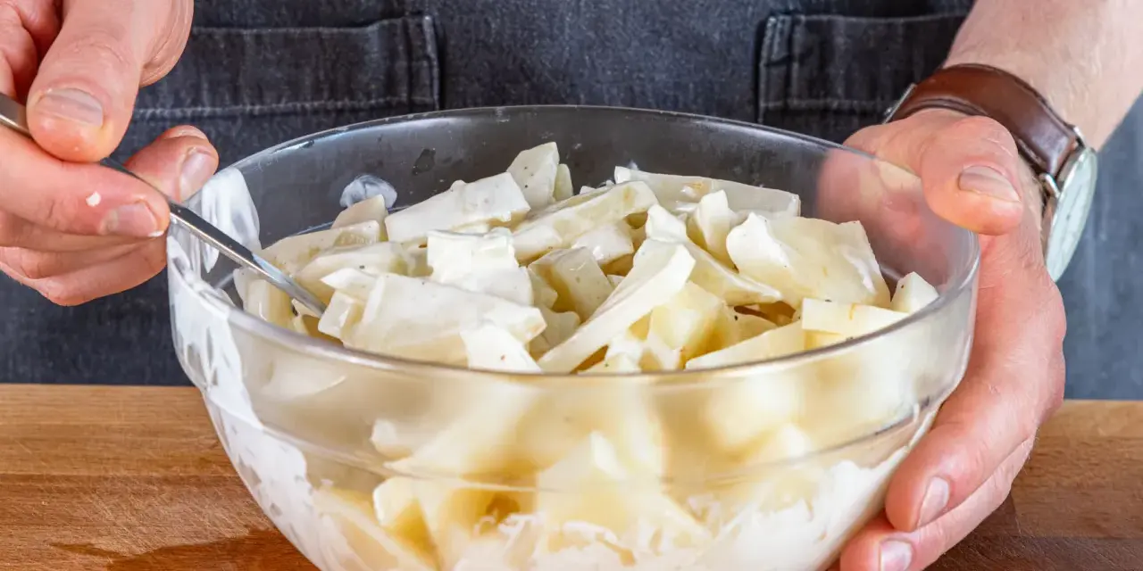 Hände mischen in einer Glasschüssel den cremigen selleriesalat nach Omas Rezept.