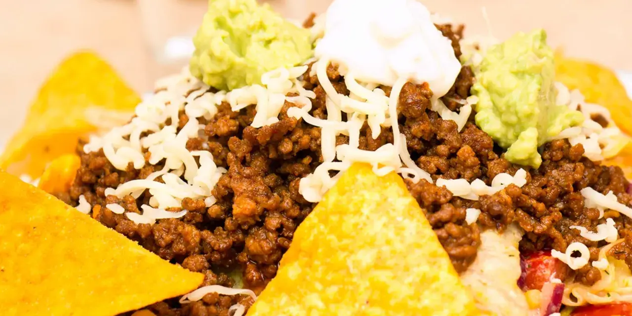 Schichtsalat mit Hackfleisch, Käse, Guacamole und saurer Sahne, garniert mit knusprigen Nachos.