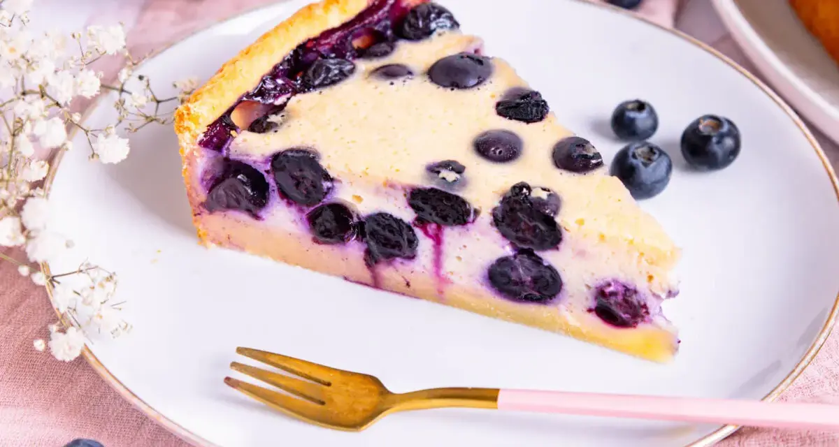 Ein Stück Blaubeerkuchen auf einem Teller, inspiriert von Landfrauen Kuchen Rezepten. Mit frischen Blaubeeren und zarter Füllung.