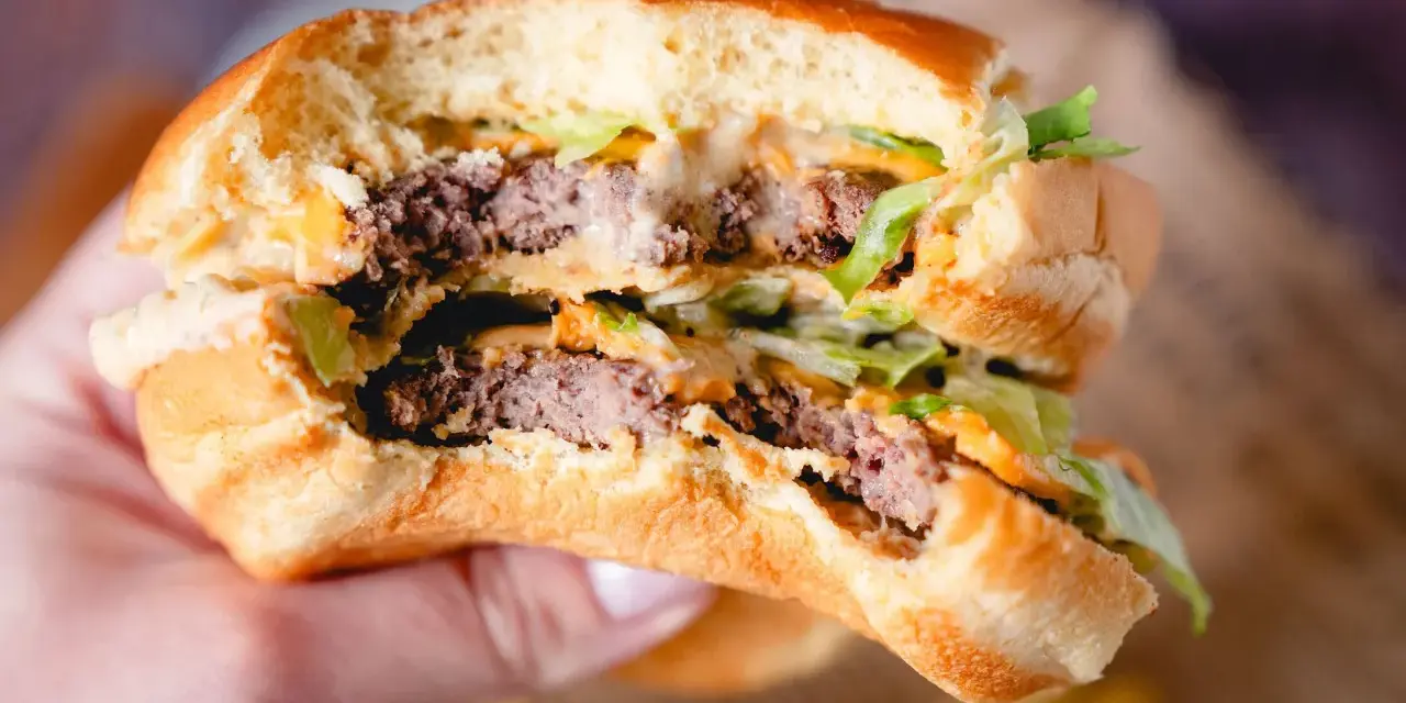 Ein saftiger Burger mit zwei Rindfleisch-Patties, Salat und der unverwechselbaren Big Mac Sauce, gehalten in einer Hand.