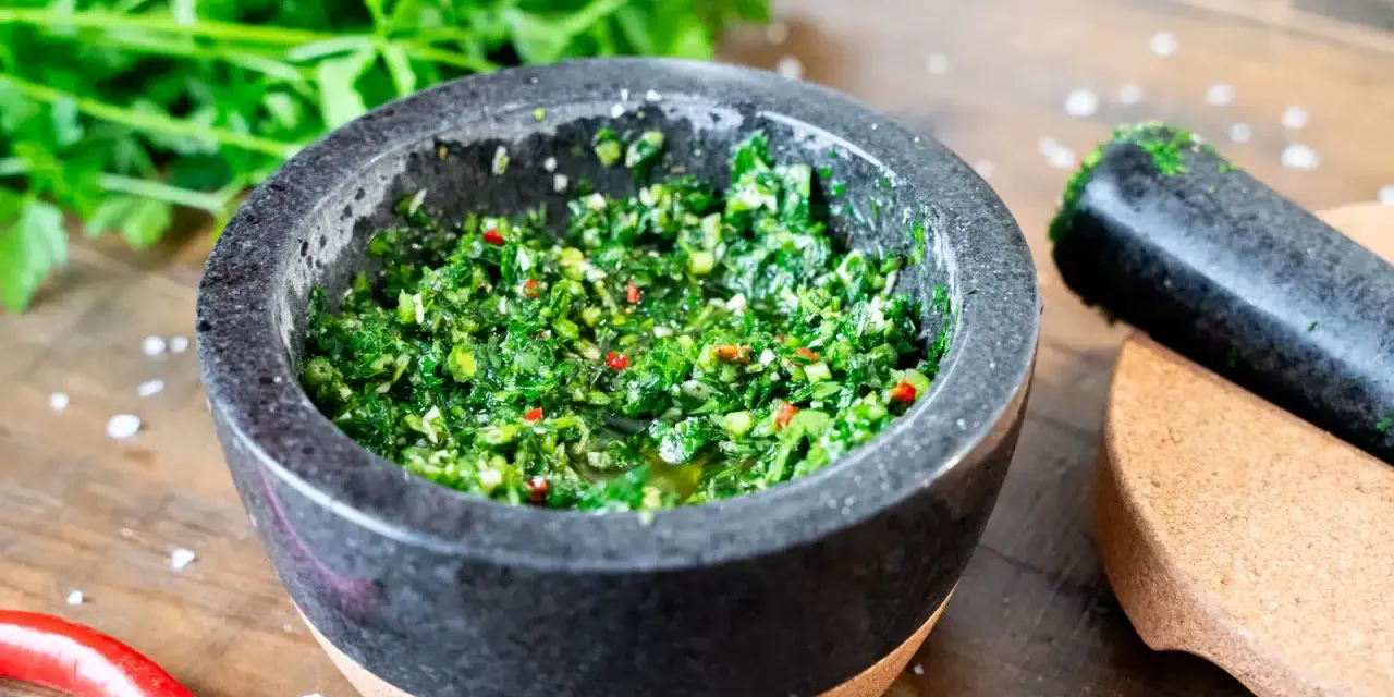 Frisches Chimichurri-Rezept im Mörser, bereit zum Verfeinern von Grillgut. Kräuter, Chili und Gewürze sind fein gehackt.