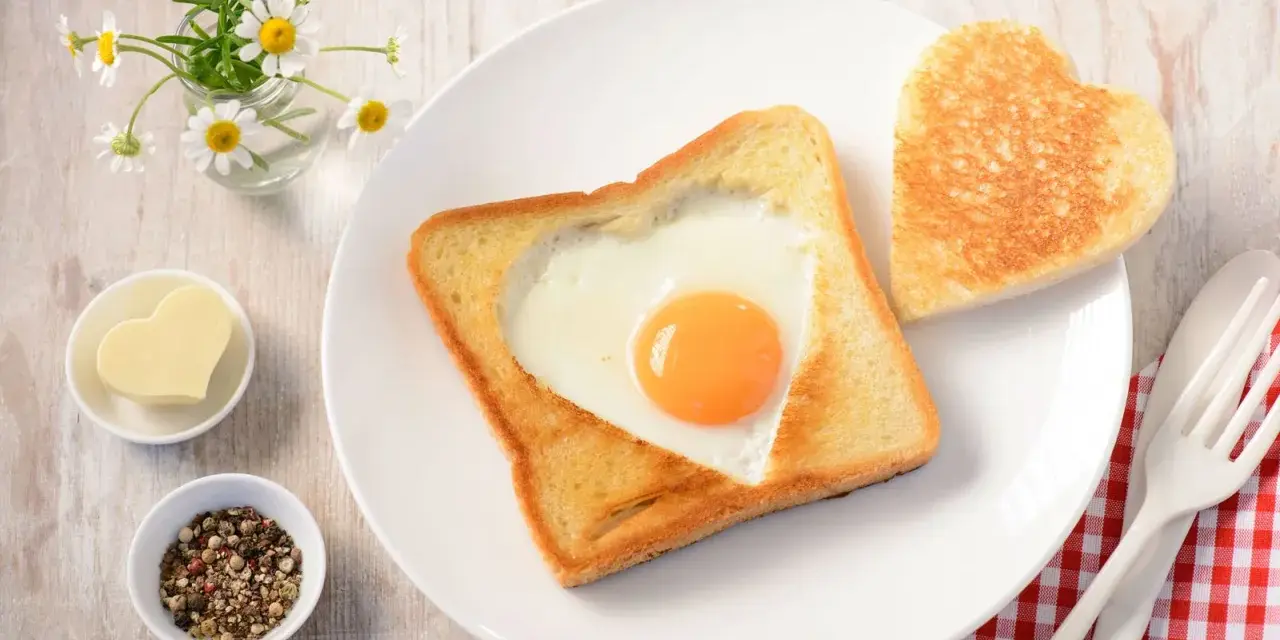 Herzförmiger Toast mit Ei, daneben ein Herzbutterstück und ein Herz-Toast. Ein liebevolles Frühstück.