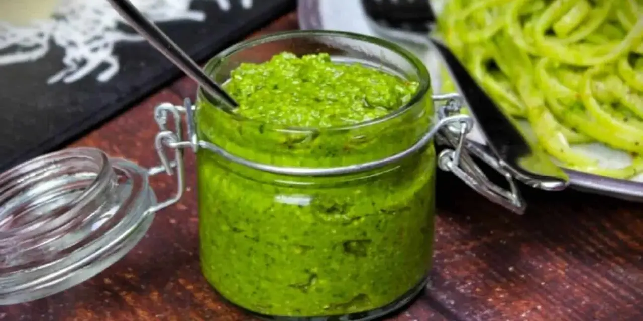 Frisches Rucola Pesto in einem Glas mit Löffel, daneben Pasta.