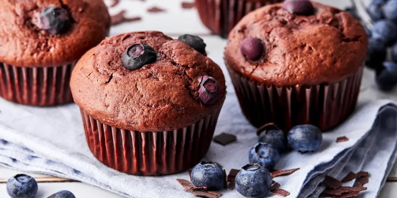 Saftige schoko blaubeer muffins, garniert mit frischen Blaubeeren und Schokostückchen, liegen auf einem Leinentuch.