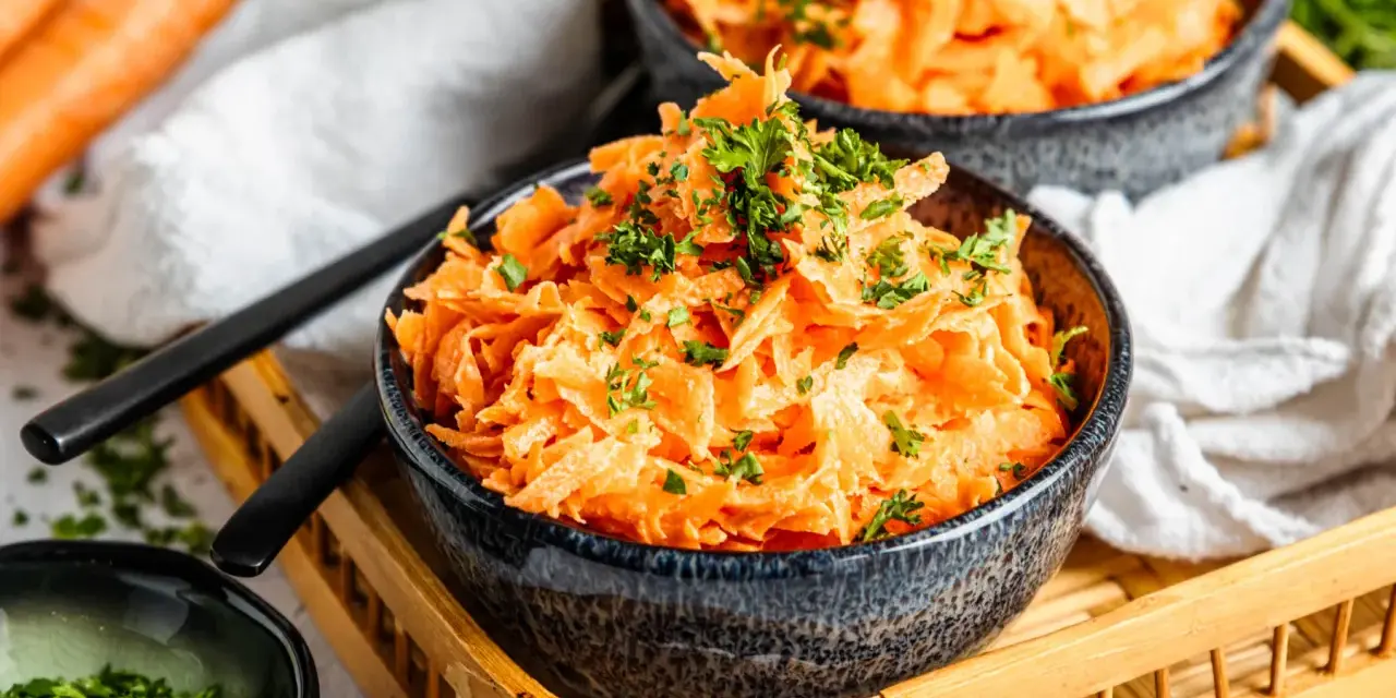 Karottensalat mit cremigem Dressing und frischer Petersilie, serviert in dunklen Schalen auf einem Holztablett.