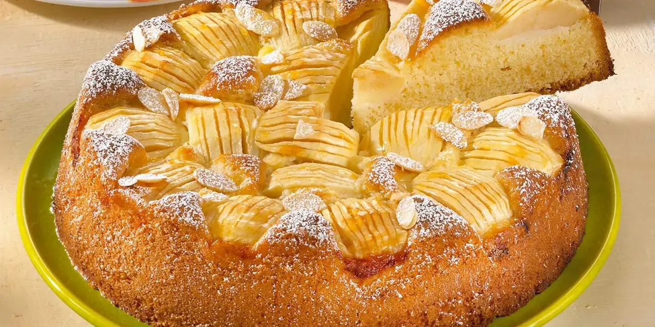 Ein saftiger, versunkener Apfelkuchen mit Mandelsplittern und Puderzucker bestreut, wird auf einem grünen Teller präsentiert.