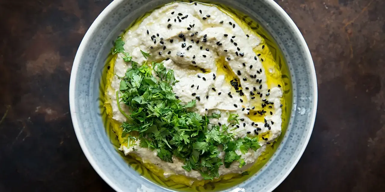 Cremiges Baba Ganoush, beträufelt mit Olivenöl, garniert mit frischer Petersilie und schwarzen Sesamkörnern.
