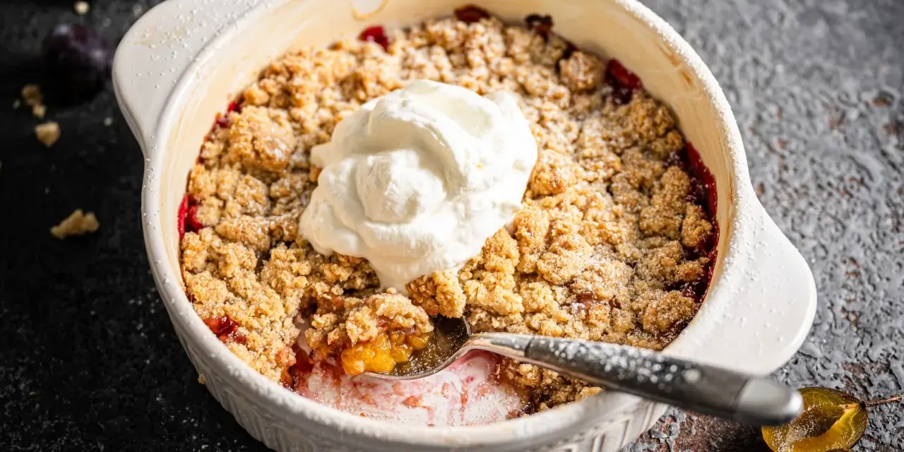 Ein köstlicher Zwetschgen Crumble mit Haferflocken, gekrönt mit einem Klecks Sahne, wartet darauf, genossen zu werden.
