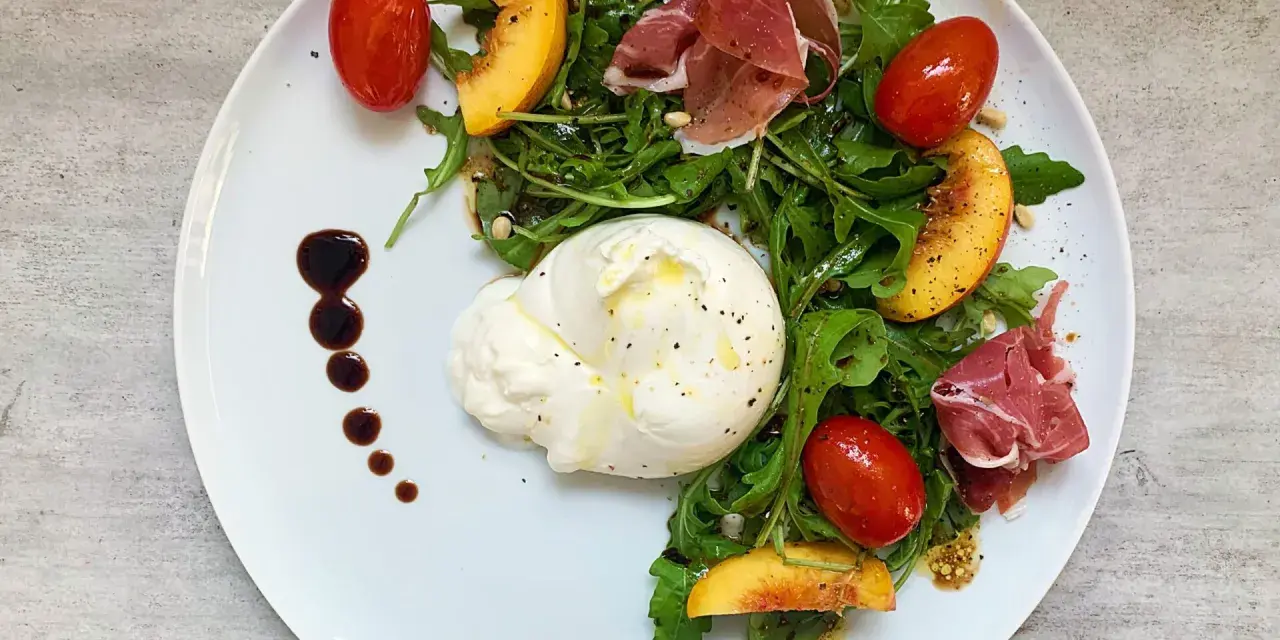 Salat mit Nektarinen, Burrata, Prosciutto und Kirschtomaten, garniert mit Balsamico-Dressing.