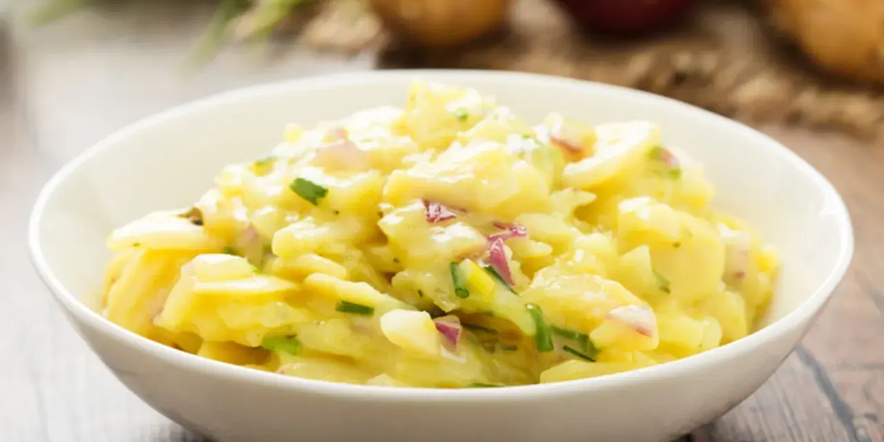 Omas Kartoffelsalat Rezept Original: Ein cremiger Kartoffelsalat mit Zwiebeln und Schnittlauch in einer weißen Schüssel, bereit zum Genießen.