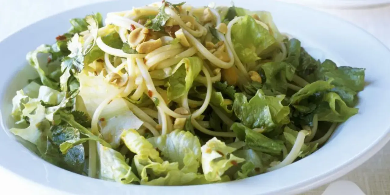 Ein leckerer Yum Yum Salat mit knackigem Eisbergsalat, Nudeln und Erdnüssen in einer weißen Schüssel.