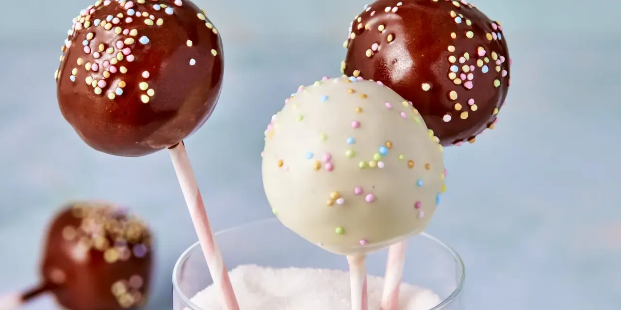 Drei bunte cake pops aus kuchenresten, mit Schokolade und Streuseln verziert, stecken in einem Glas voller Zucker.