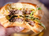 Ein saftiger Burger mit zwei Rindfleisch-Patties, Salat und der unverwechselbaren Big Mac Sauce, gehalten in einer Hand.