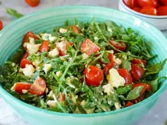 Frischer Rucolasalat mit saftigen Tomaten und cremigem Käse in einer türkisfarbenen Schüssel.