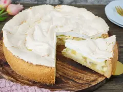 Ein saftiger Rhabarberkuchen mit luftigem Baiser, ein Stück davon ist bereits angeschnitten.