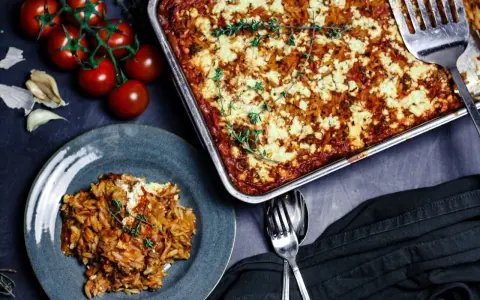 Herzhafter Kritharaki Auflauf mit Hackfleisch und Feta, garniert mit Thymian. Daneben frische Tomaten und Knoblauch.